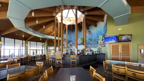 A restaurant with a central bar, wooden tables and chairs, and a mural of underwater scenery on the walls.