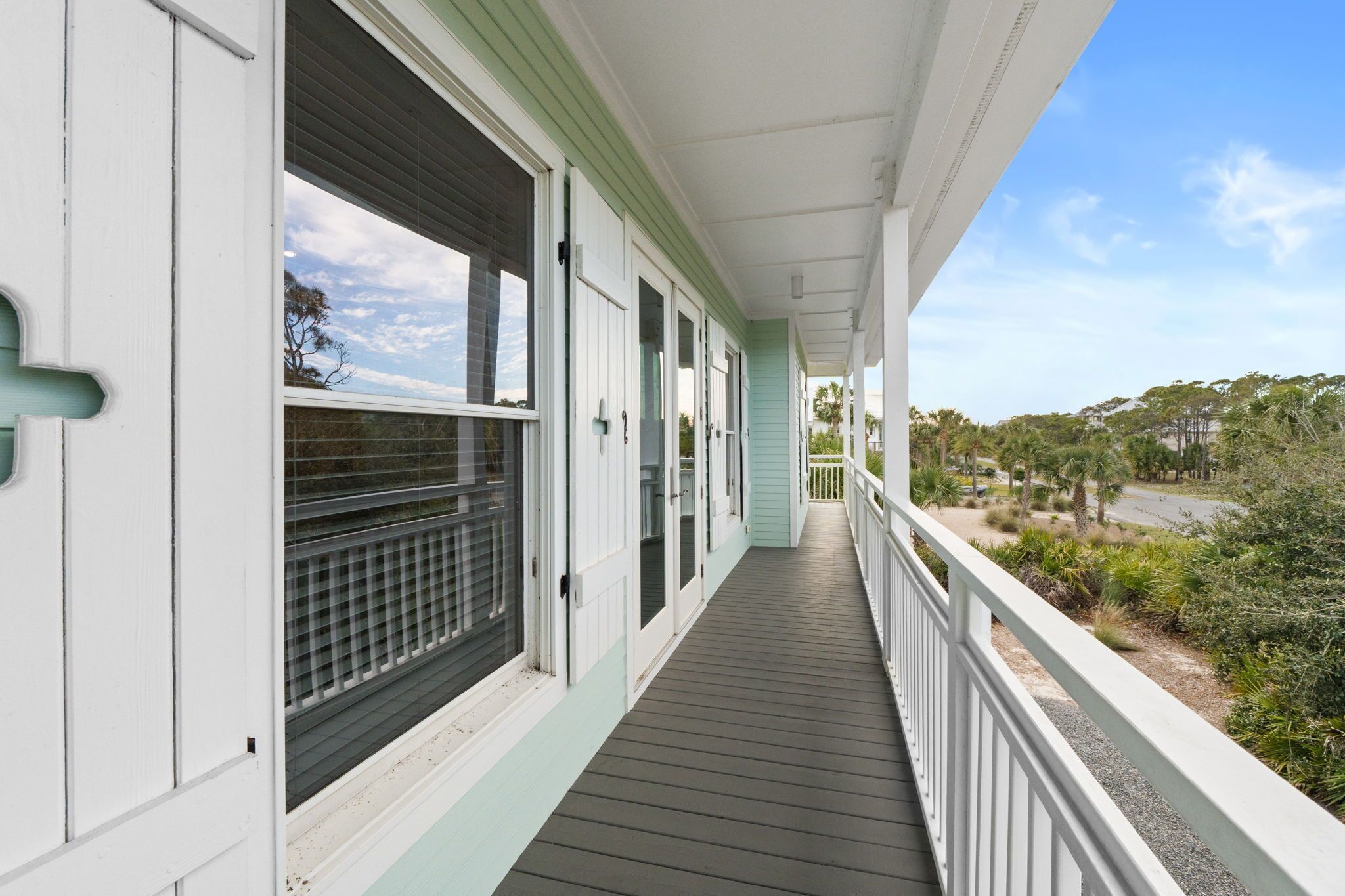 A covered wooden deck with a railing, leading to a building with white and green trim and multiple windows.