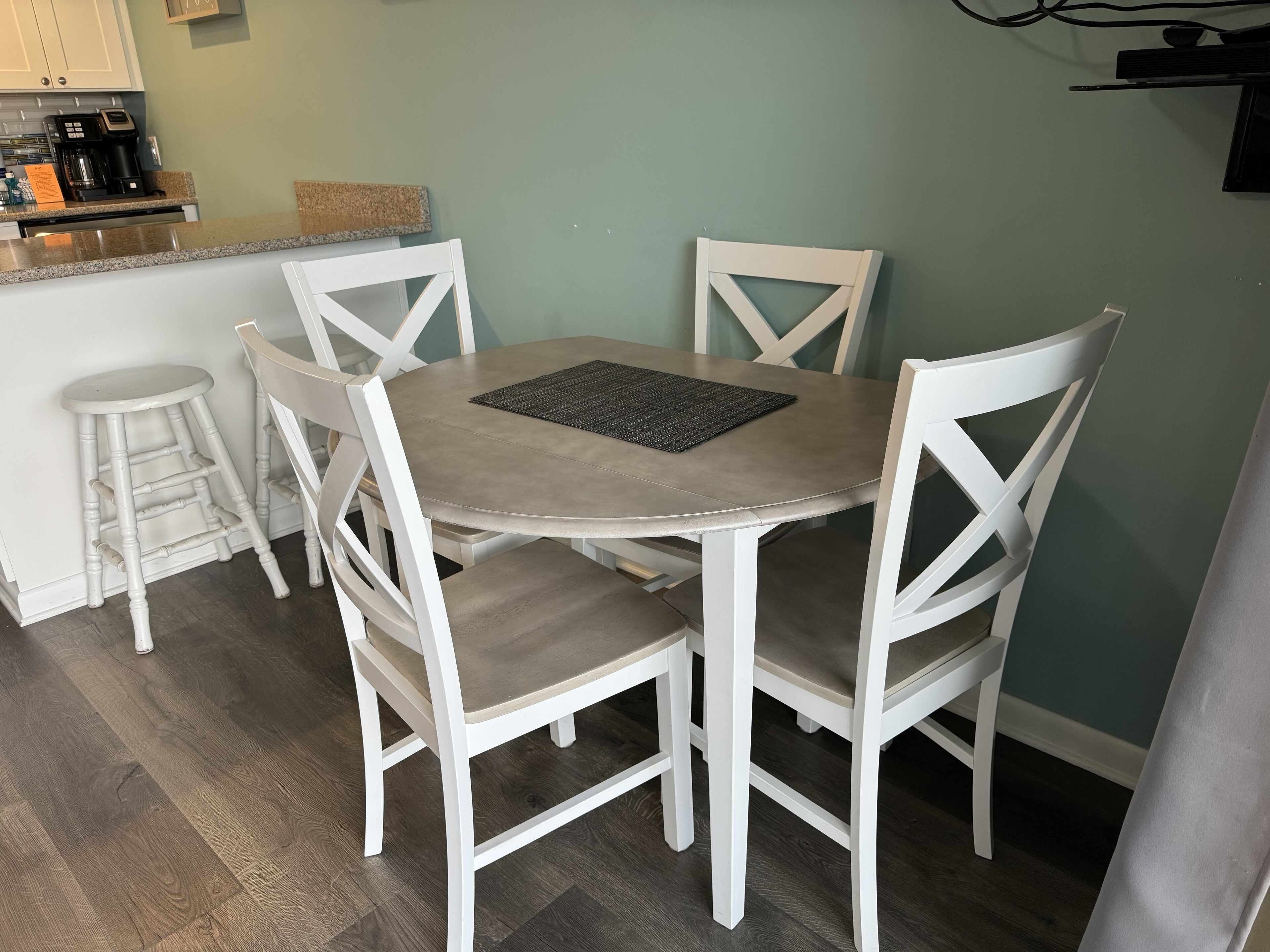 Un comedor con una mesa redonda, cuatro sillas blancas y una cafetera sobre el mostrador.