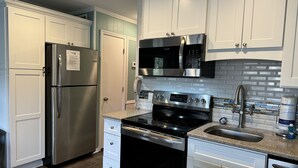 A modern kitchen with white cabinets, stainless steel appliances, a granite countertop, and a tiled backsplash.