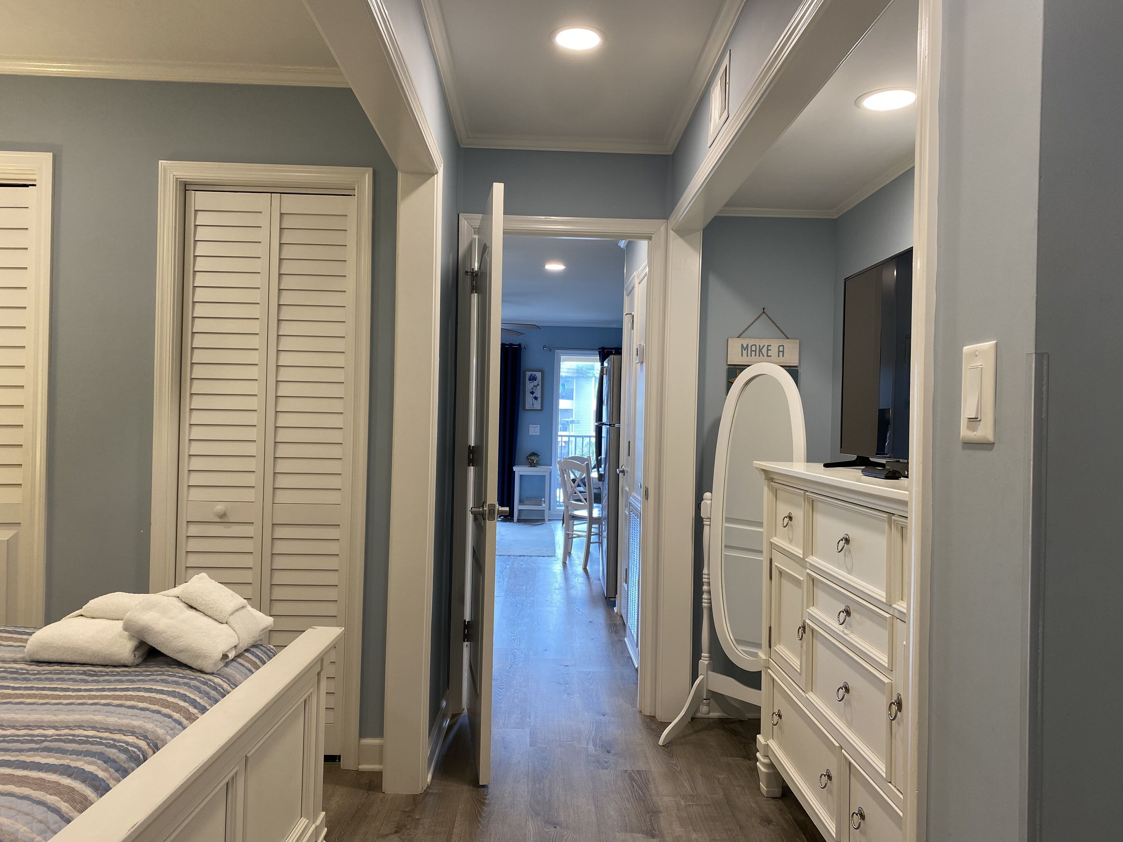 A bedroom with a bed, a dresser, a mirror, and a hallway leading to a balcony.