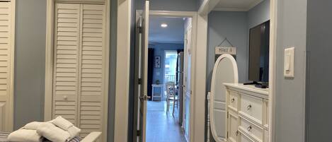 A bedroom with a bed, a dresser, a mirror, and a hallway leading to a balcony.