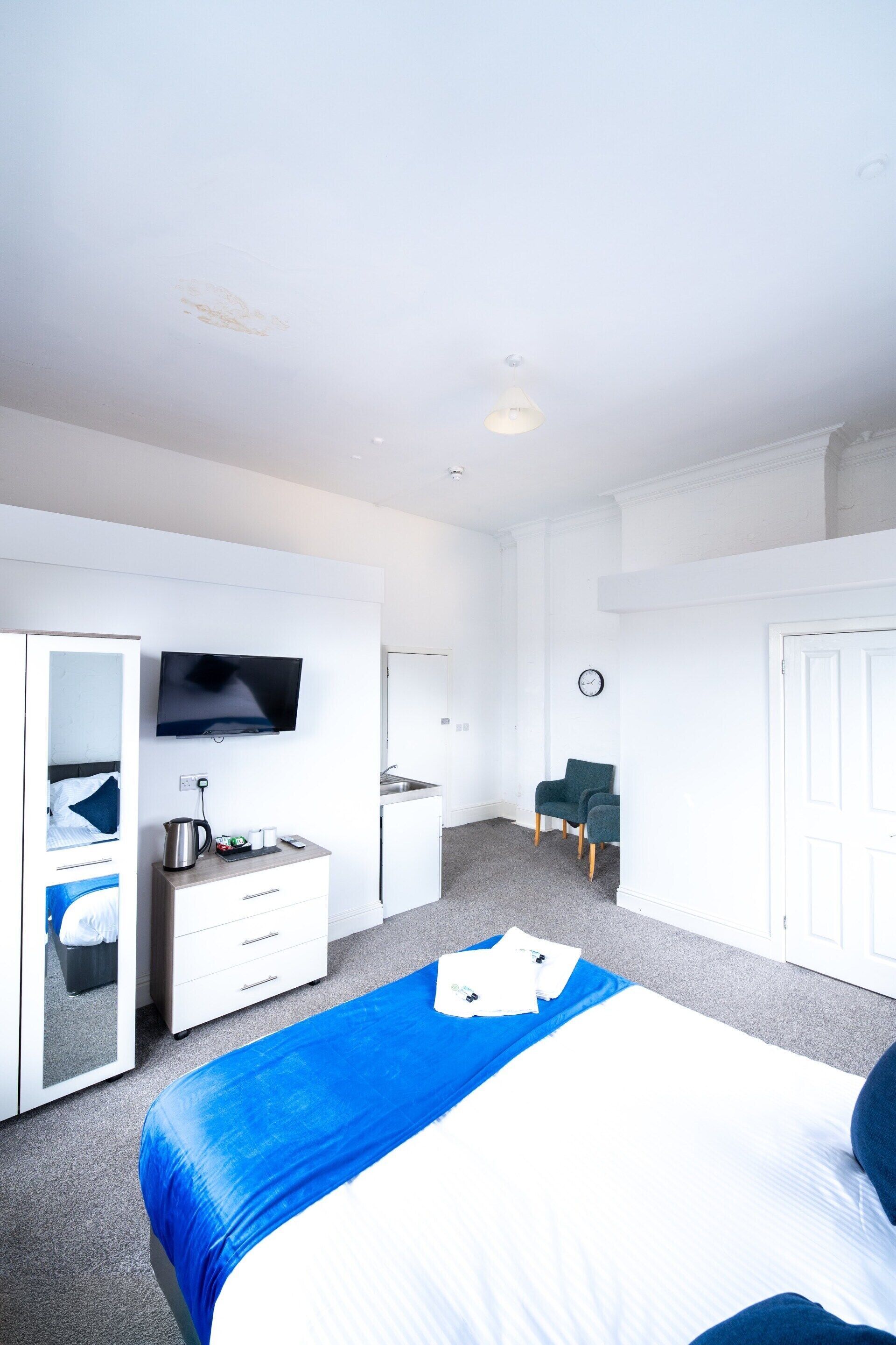 A hotel room with a bed, a TV, a desk with a kettle, a chair, and a wardrobe.