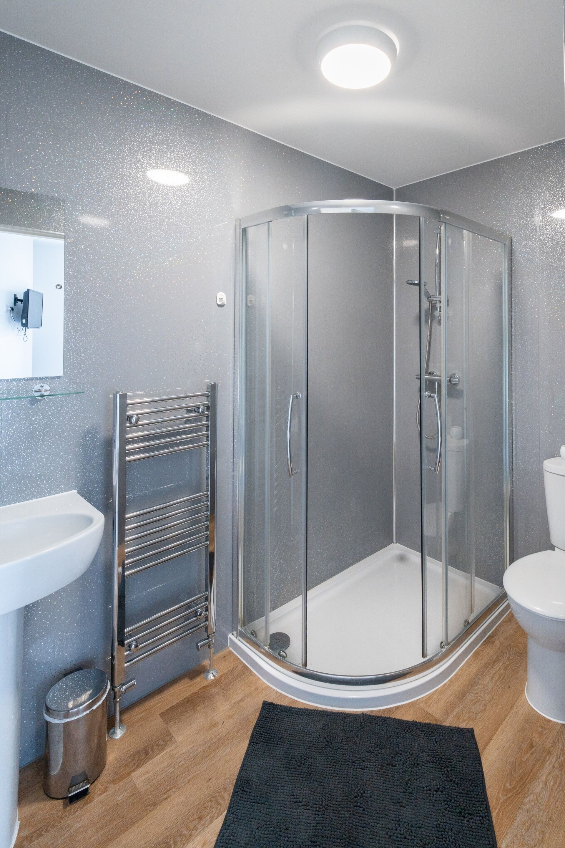 Un baño moderno con cabina de ducha de vidrio, un lavamanos blanco y un inodoro.