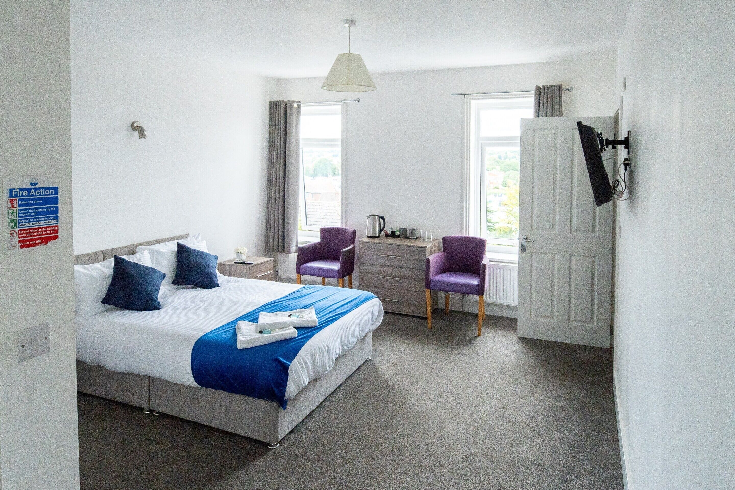 A hotel room with a bed, two chairs, a desk, a TV, and a window.