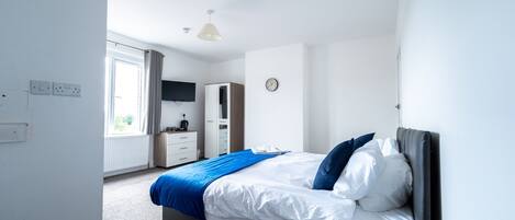 A modern bedroom with a bed, a window, a wardrobe, and a clock on the wall.