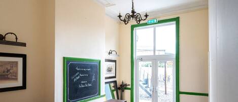 A reception area with a wooden reception desk, a chalkboard with writing, a door with a green frame, and a staircase leading outside.