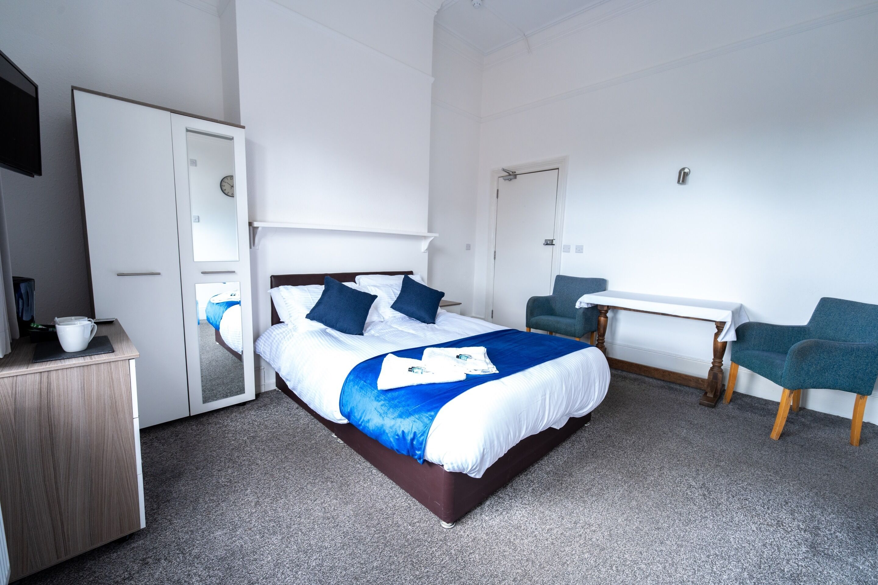 Une chambre d’hôtel avec un lit, un bureau, une chaise et une armoire.