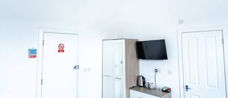Habitación de hotel con cama, escritorio con televisor de pantalla plana, armario y puerta con letrero de prohibido fumar.