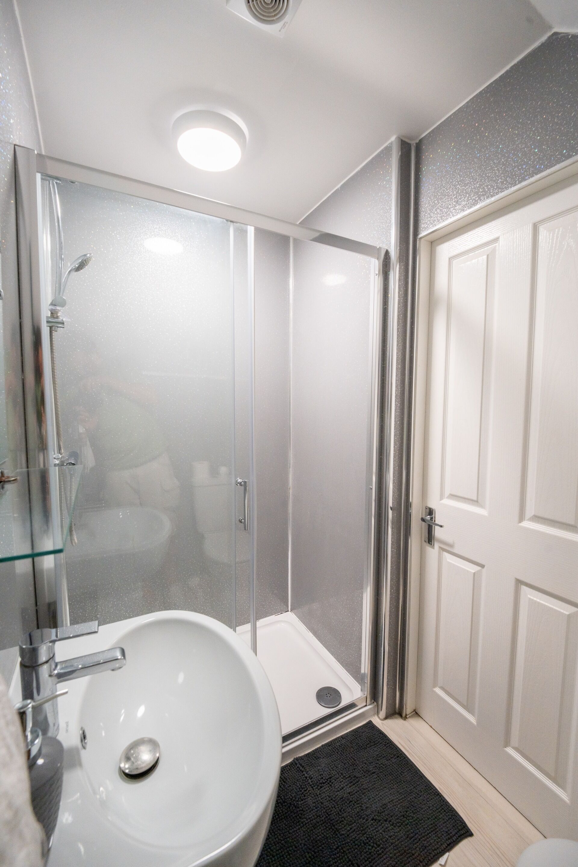 Une salle de bain avec une douche à parois de verre, un lavabo blanc et une porte.