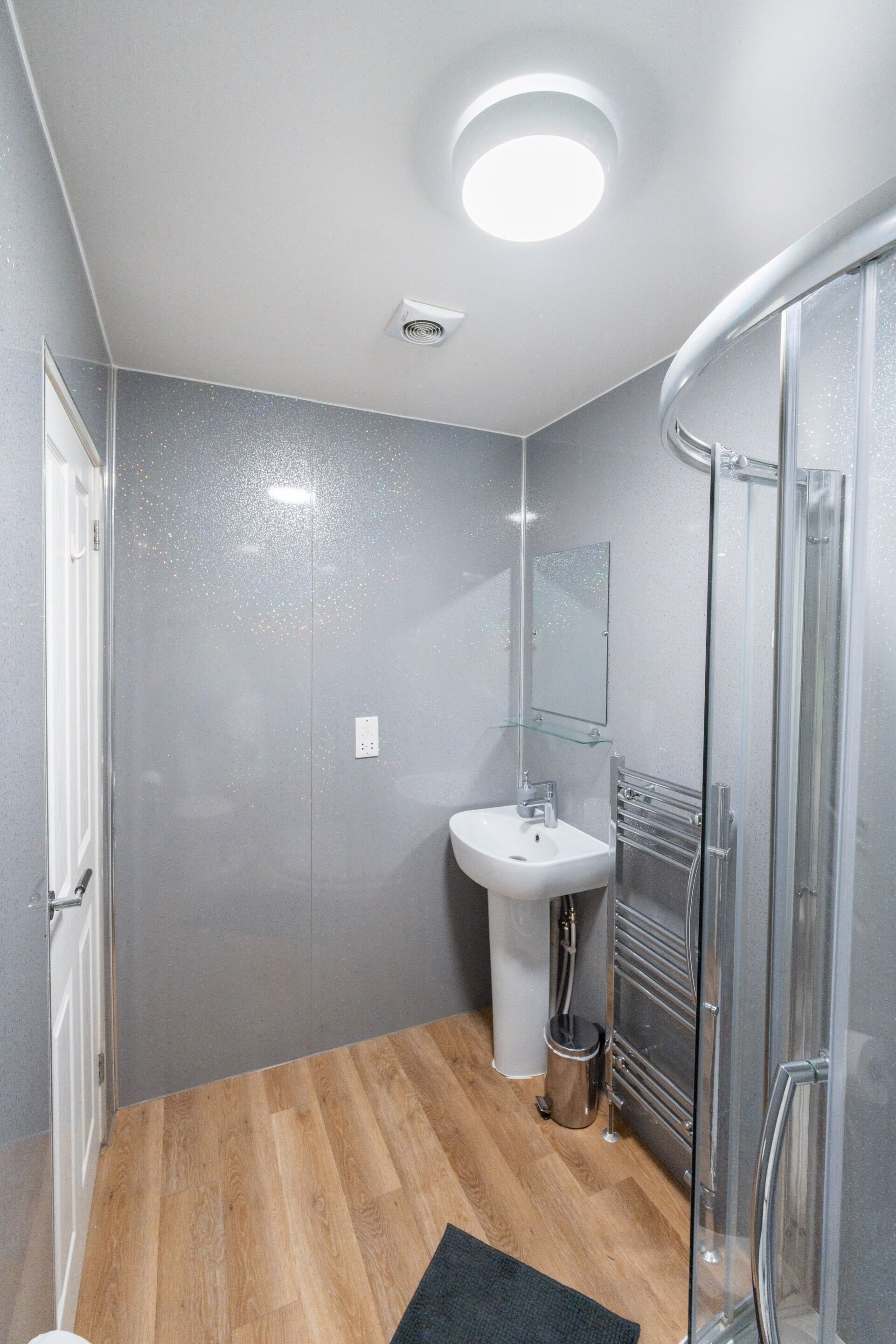 A bathroom with a glass shower enclosure, a pedestal sink, and a mirror on the wall.
