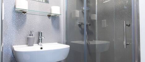A modern bathroom with a glass-enclosed shower, a pedestal sink, and a mirror above the sink.