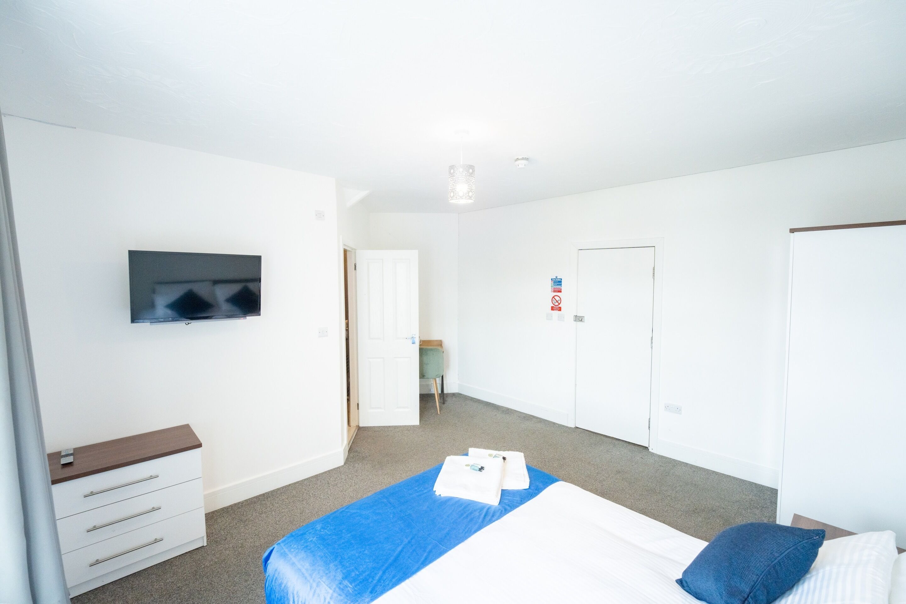 A bedroom with a bed, a TV mounted on the wall, a dresser, and a door with a sign.