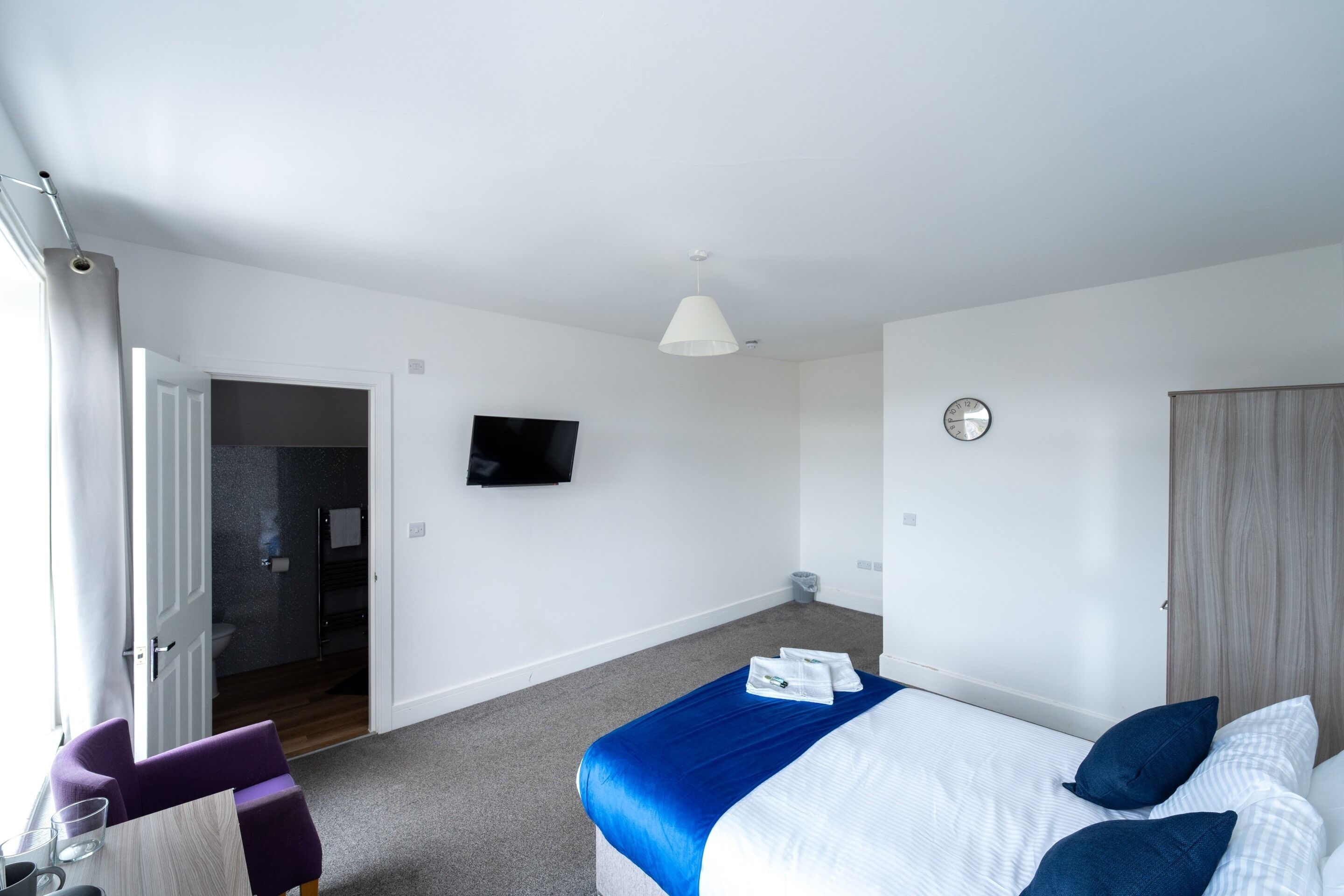 A hotel room with a bed, a TV, a door leading to a bathroom, and a small table with a chair.