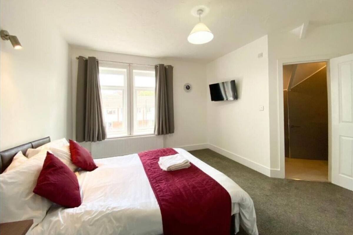 Ett hotellrum med en säng, gardiner, en platt-TV och en dörr som leder till ett annat rum.