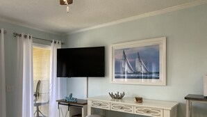 A room with a white desk, two chairs, a TV, and a framed picture of sailboats. - Ocean View - Ocean Villas A322- Professionally Managed by HHB&T Vacation Rentals (Hilton Head Island)