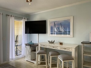 Une pièce avec un bureau blanc, deux chaises, un téléviseur et un tableau représentant des voiliers.