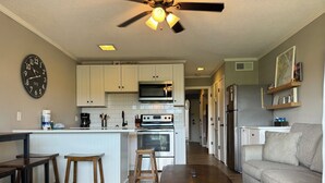 A modern kitchen with white cabinets, a microwave, and a stove. There is a dining area with wooden stools and a table. A ceiling fan is visible above the kitchen. - Resort View - Ocean Villas A336-Professionally Managed by HHB&T Vacation Rentals (Hilton Head Island)