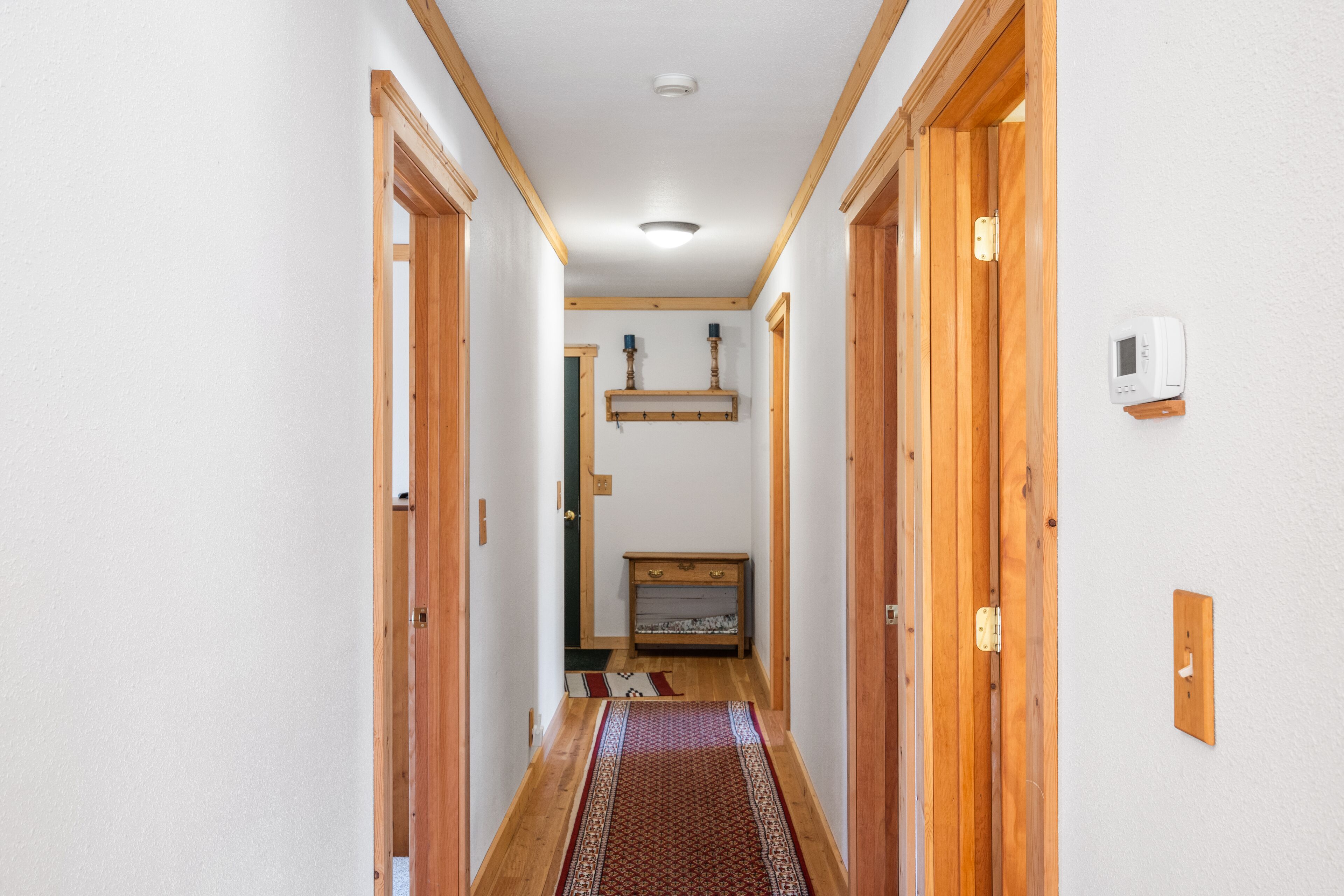 A narrow hallway with wooden doors and a patterned rug on the floor.