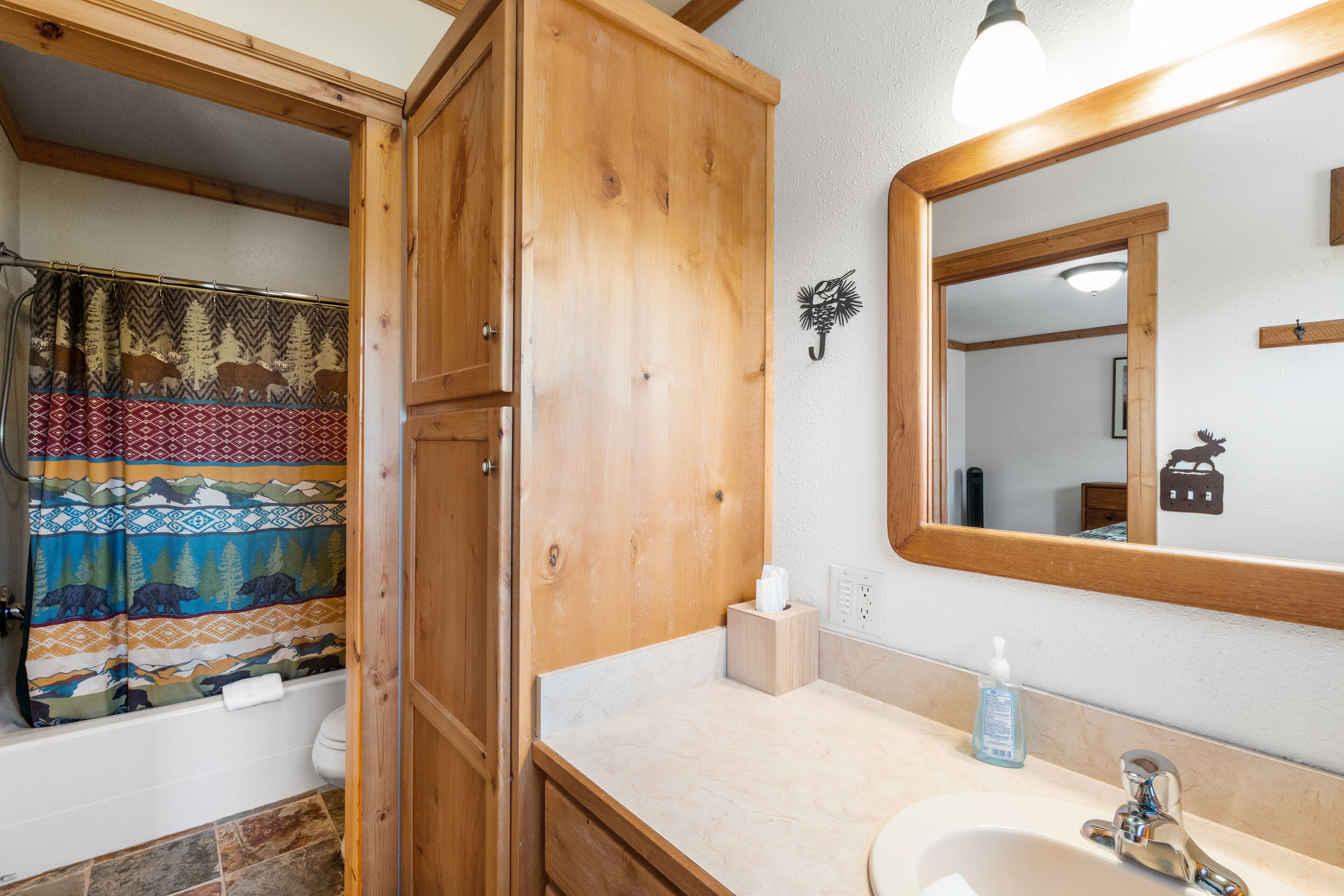 A bathroom with a wooden cabinet, a shower curtain with a bear pattern, a mirror, and a sink with a soap dispenser.