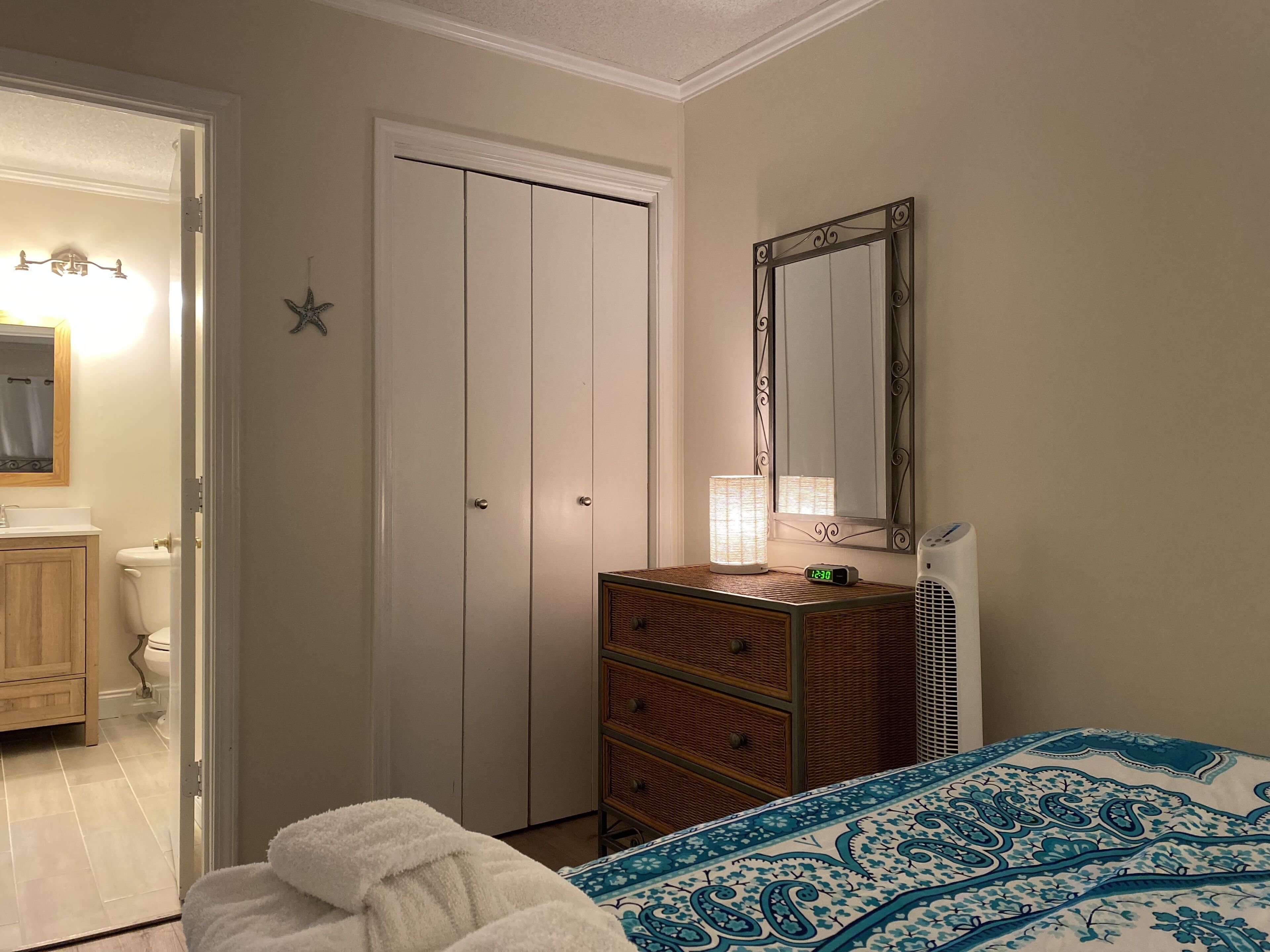 A bedroom with a bed, a dresser, a mirror, and a door to the bathroom.
