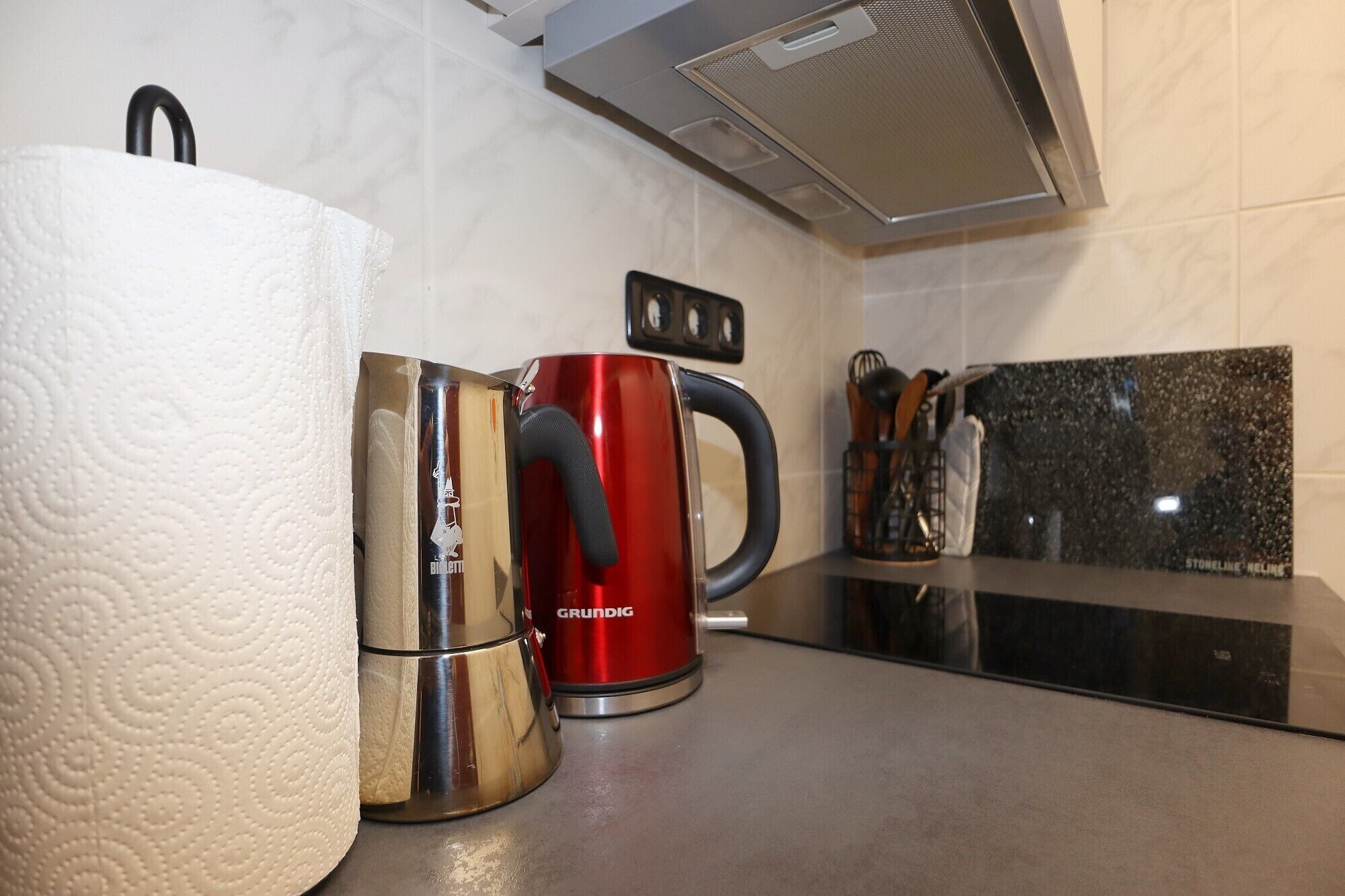 A kitchen with a stainless steel kettle, a roll of paper towels, and a coffee maker.