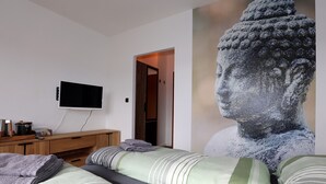 Une chambre à coucher comprenant un lit, un téléviseur, une commode en bois et une grande statue.