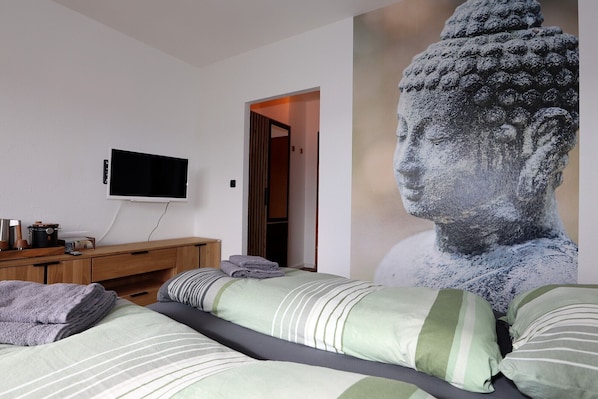 A bedroom with a bed, a television, a wooden dresser, and a large statue. - Carpediem Apartments (Schoenwald)