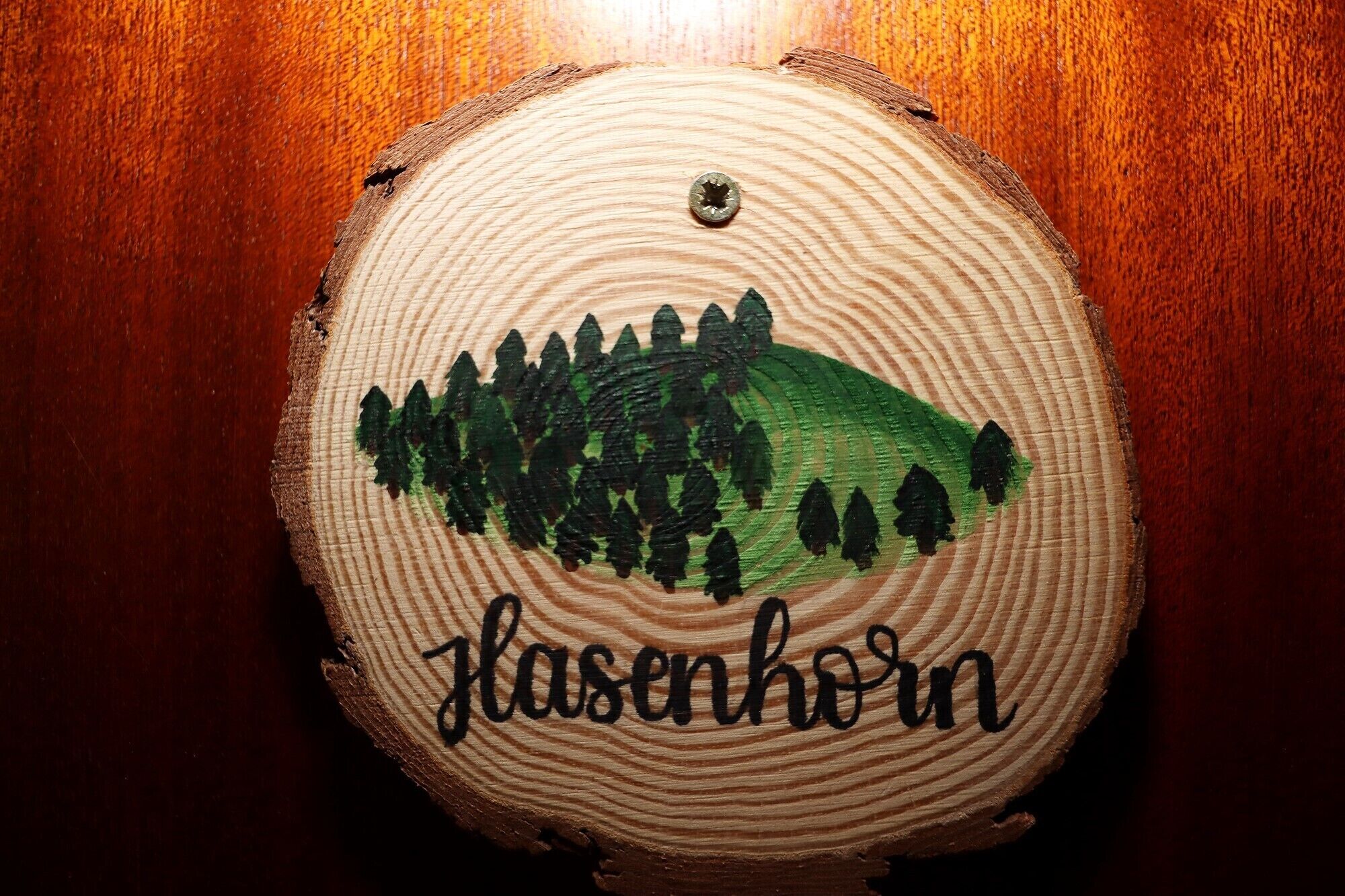 A wooden coaster with a painted landscape and the word 'Flasenkorn' on it.
