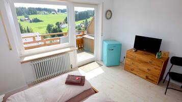A bedroom with a bed, a dresser, a television, and a view of a balcony.