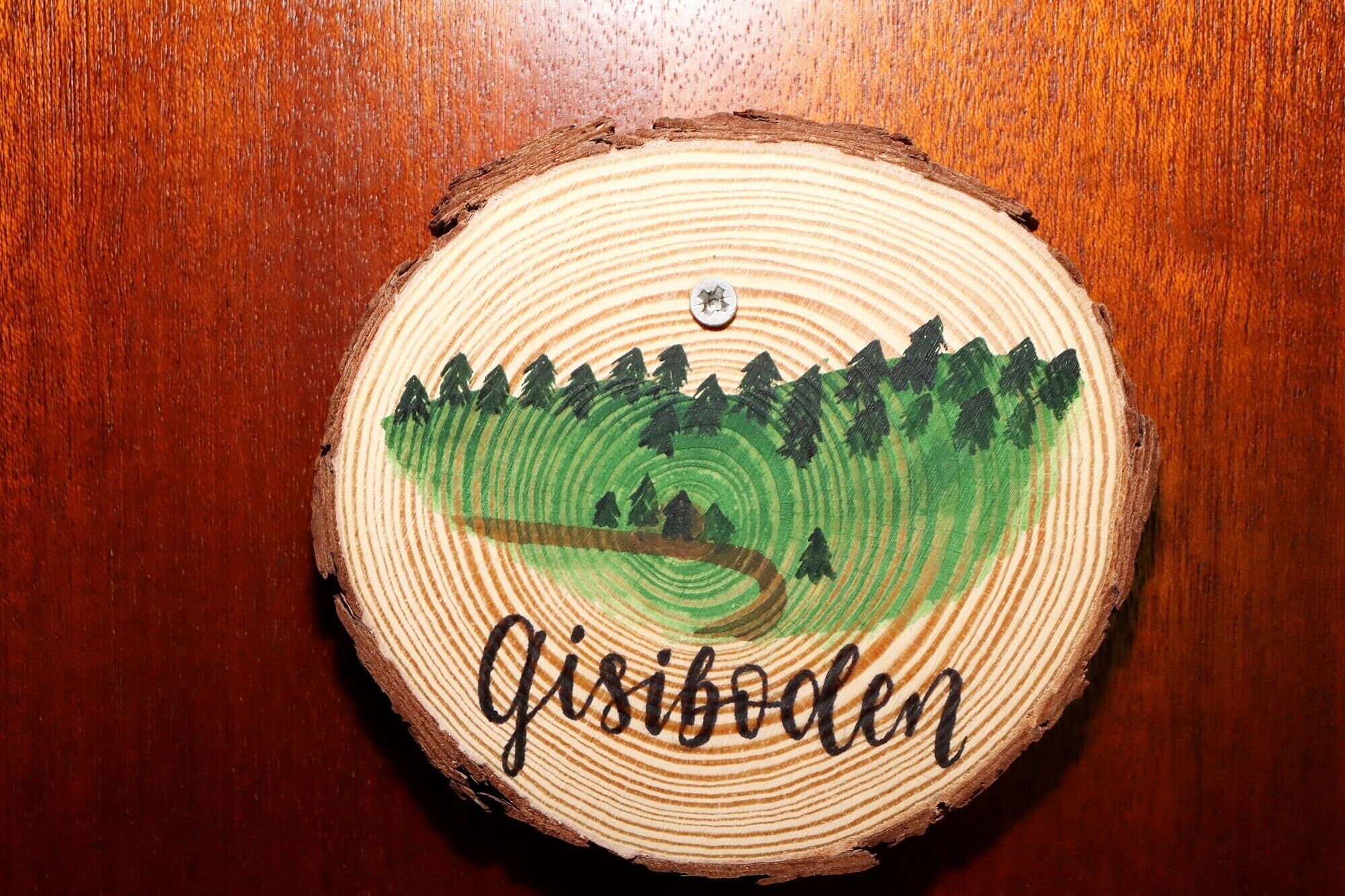 A wooden coaster with a painted landscape and the word 'Gisibolen' on it.