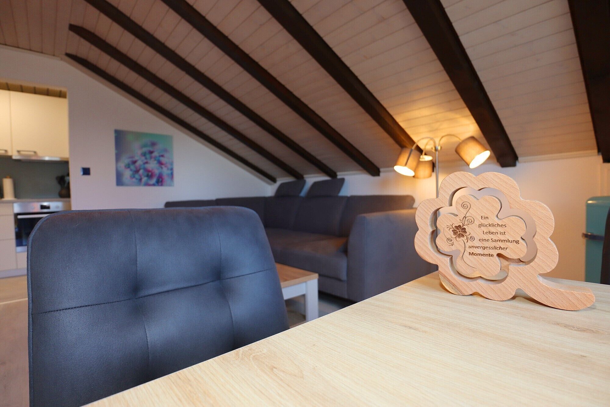 A modern living room with a sofa, a dining table, and a wooden decorative piece with text.