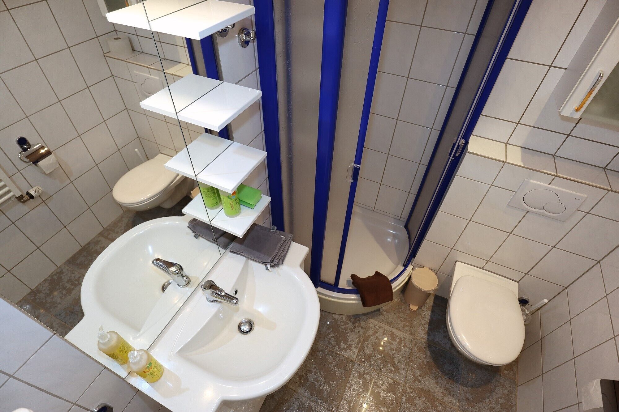 Une salle de bain avec un lavabo blanc, deux toilettes, un espace douche et un porte-serviettes.