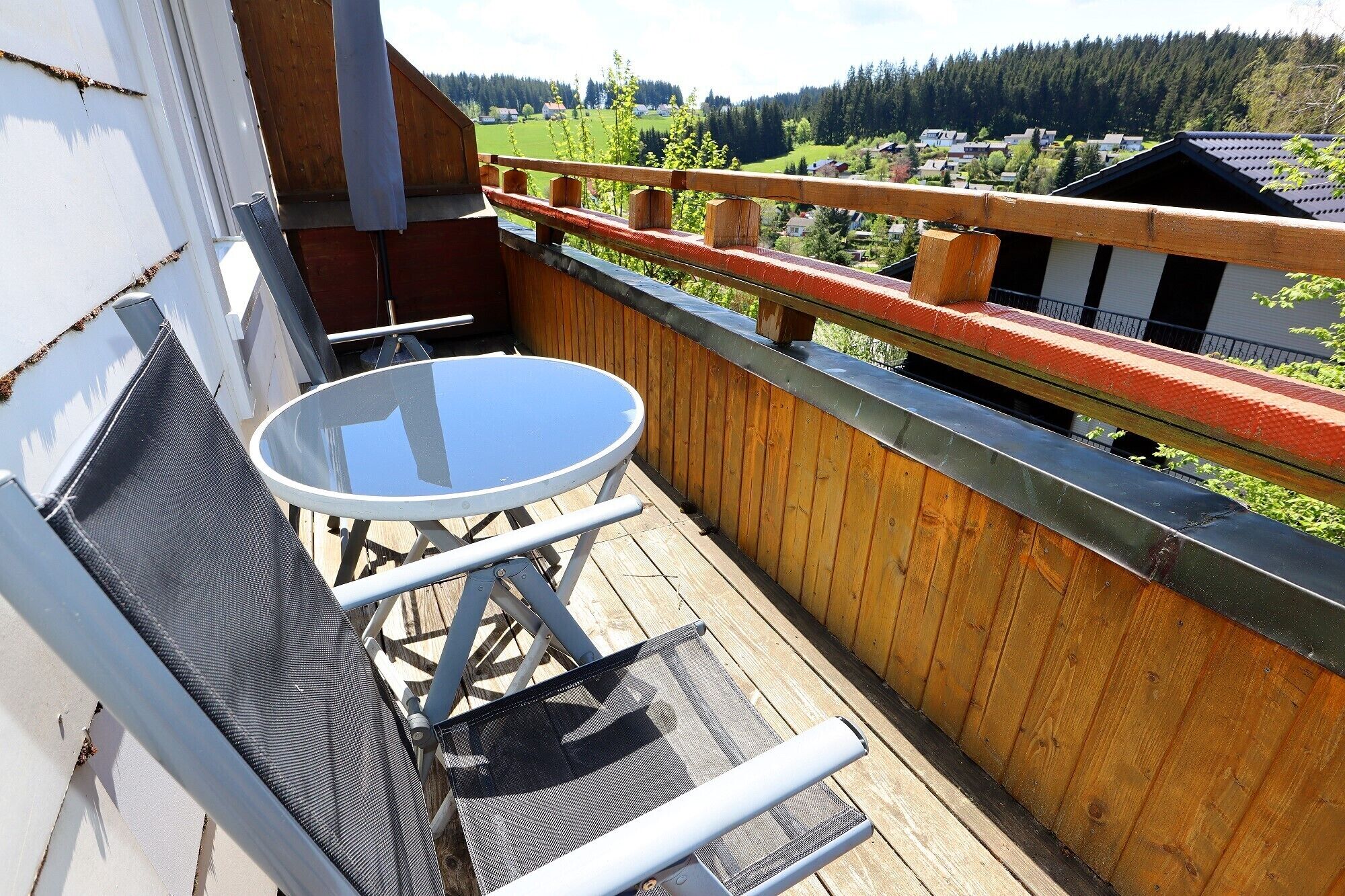 Un balcón con mesa y sillas, con vistas a una zona residencial con casas y árboles.