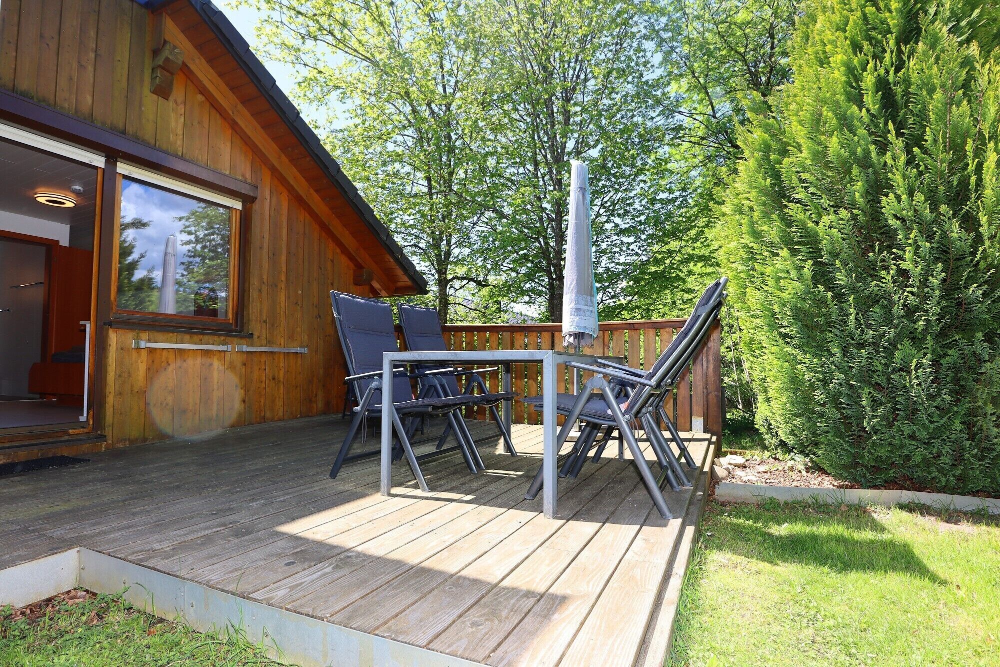Une terrasse en bois avec une table et des chaises, un parasol et un chalet en bois doté d’une fenêtre.