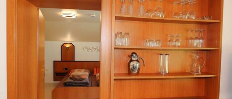 A wooden cabinet with shelves holding various glassware and a silver pitcher.
