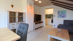 Un salon moderne avec un téléviseur, des sièges et une cuisine en arrière-plan.