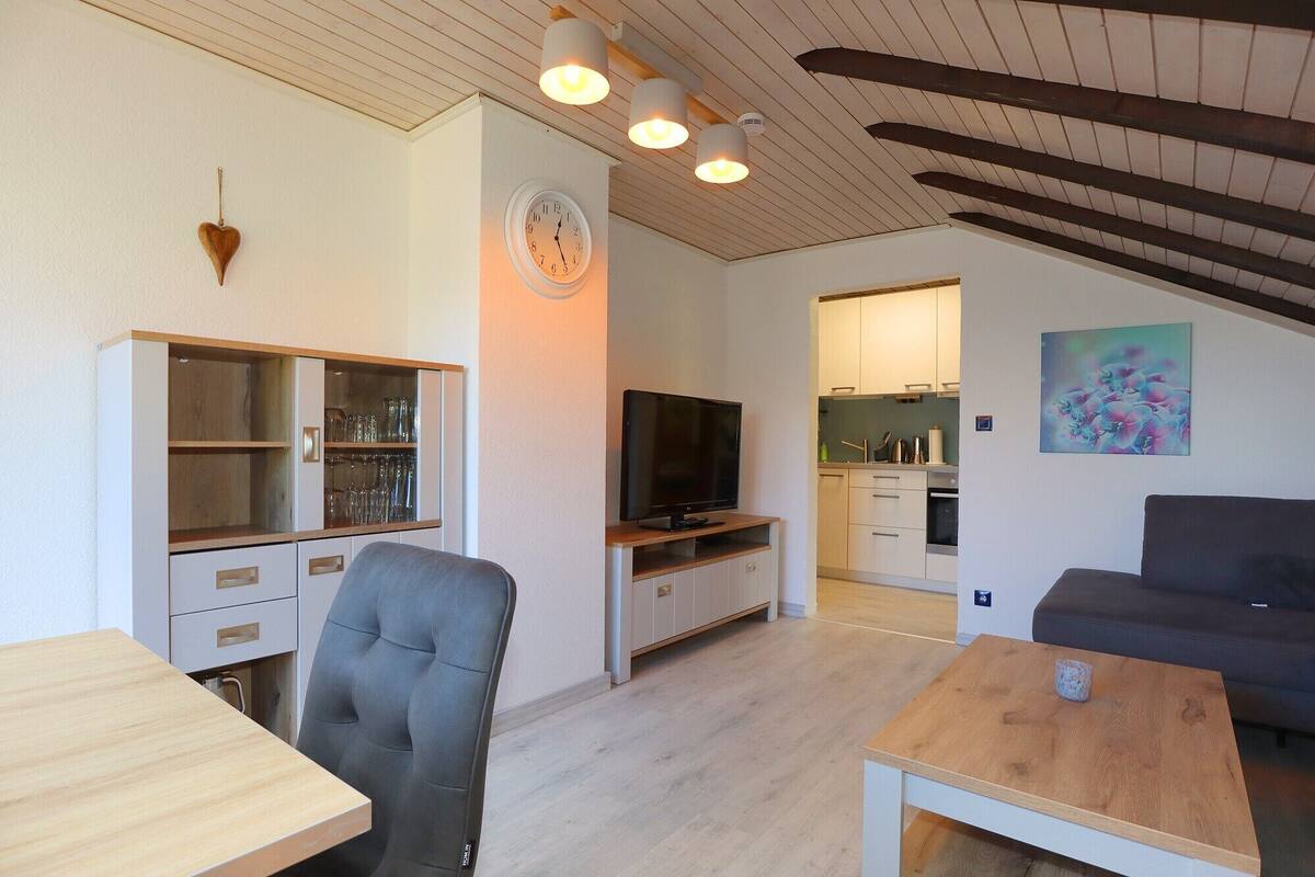 A modern living room with a TV, seating, and a kitchen in the background.