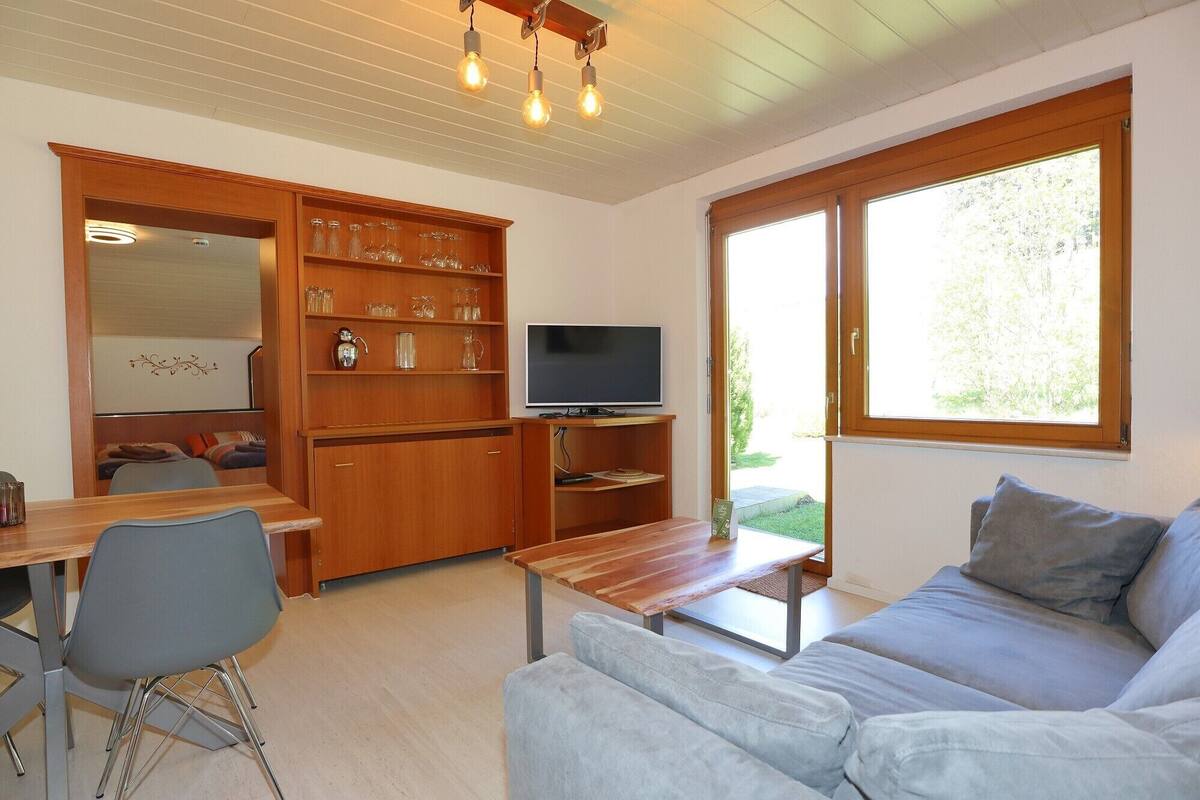 A modern living room with a wooden TV stand, a sofa, a dining table with chairs, and a built-in shelving unit with glassware.