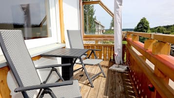 Een houten terras met een tafel en stoelen, uitzicht op een gebouw, en een houten balustrade.
