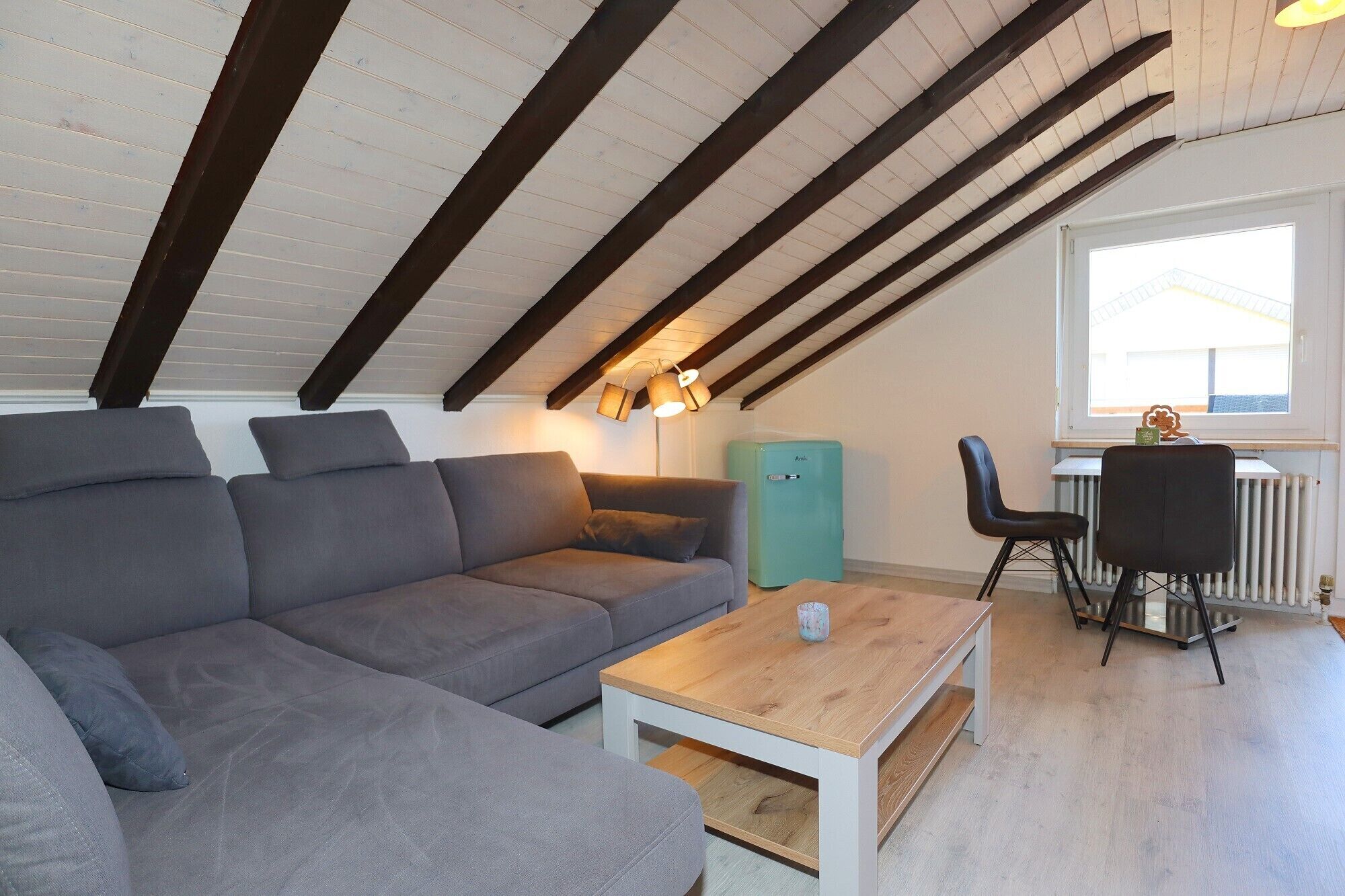 A modern loft bedroom with a sloped ceiling, a grey sofa, a wooden coffee table, and a radiator.