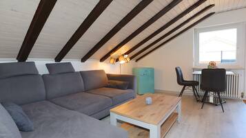 A modern loft bedroom with a sloped ceiling, a grey sofa, a wooden coffee table, and a radiator.
