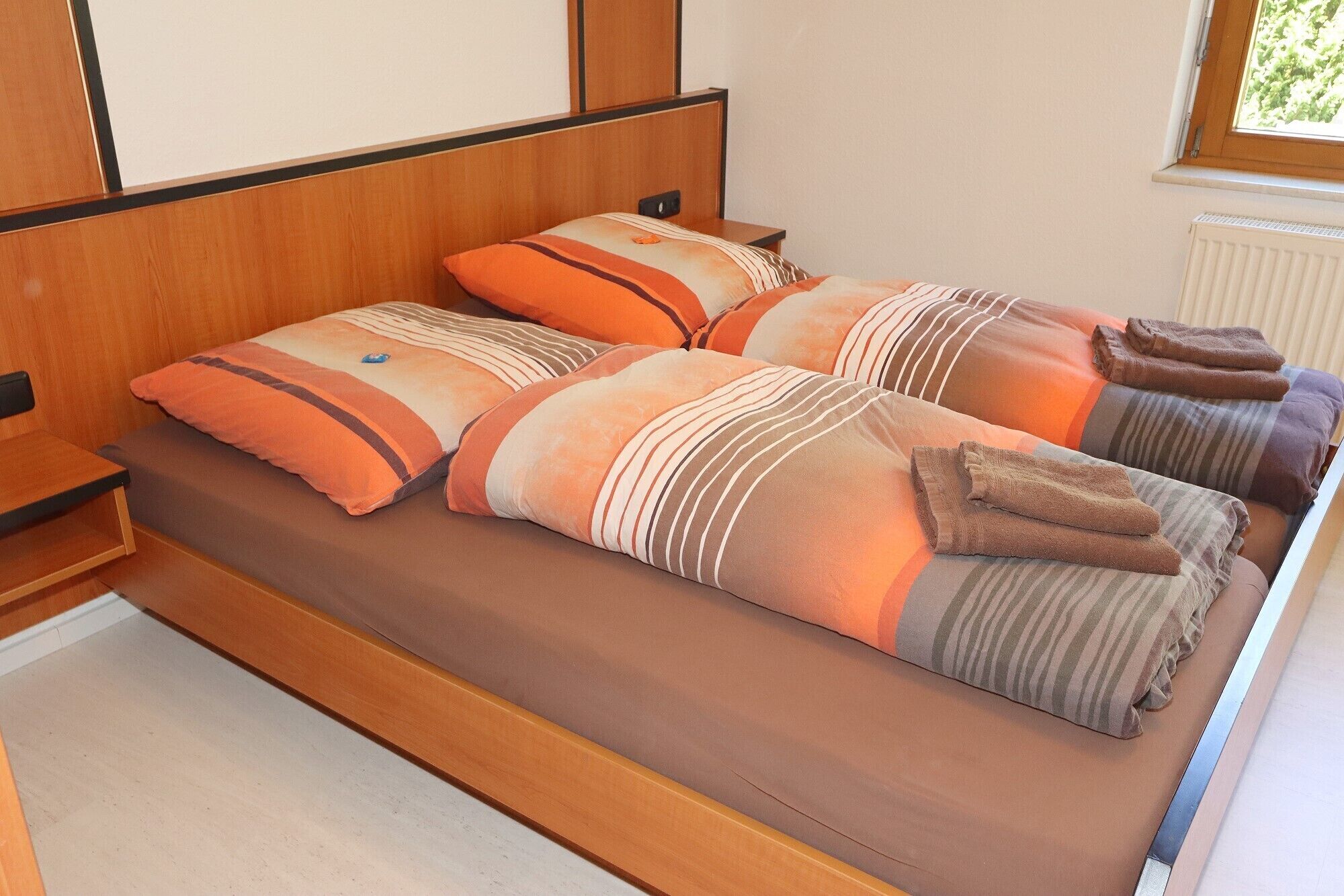 A double bed with striped bedding and two pillows, a wooden headboard, and a window with blinds.
