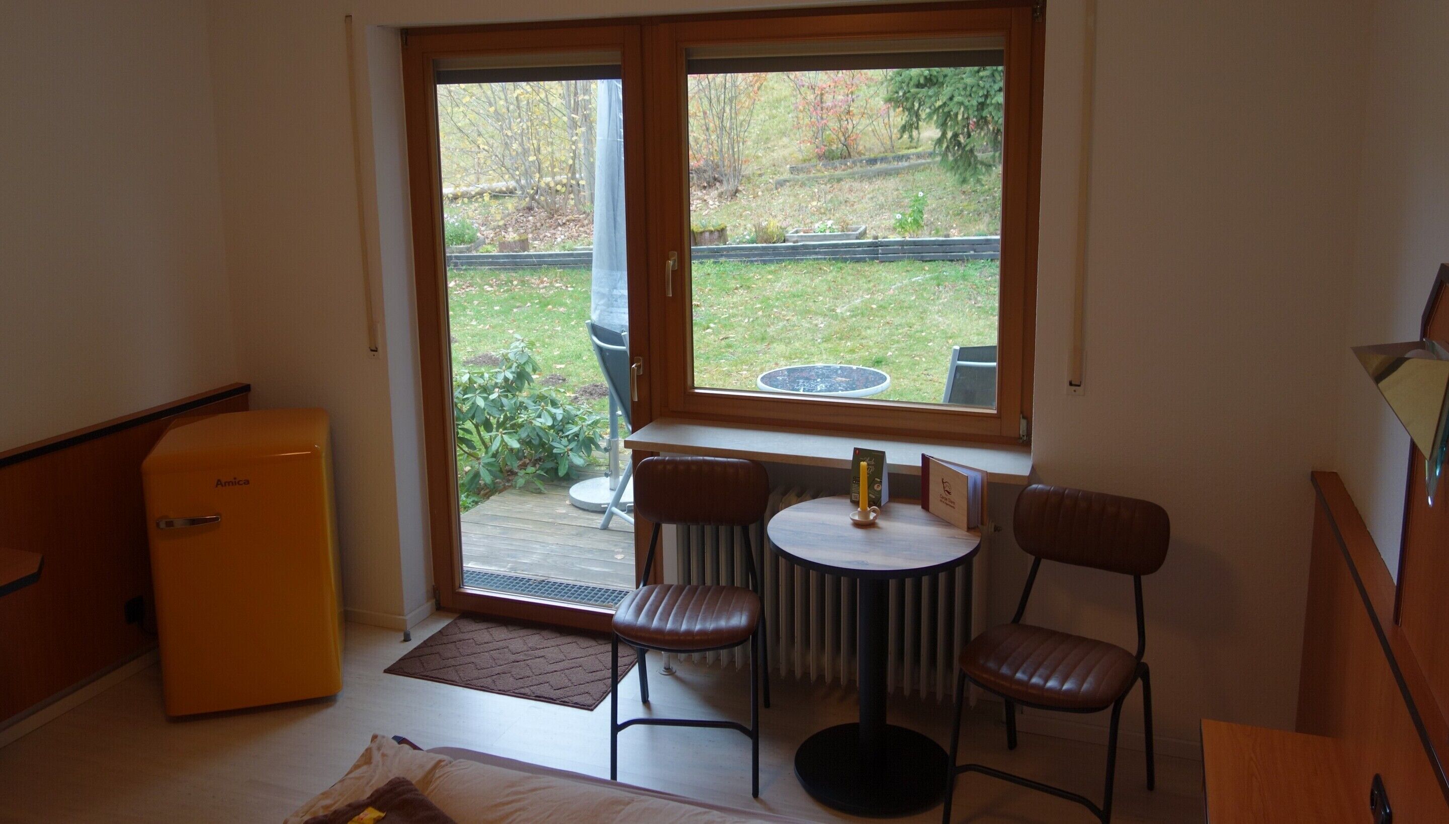 A compact room with a small table and two chairs, a radiator, and a sliding glass door leading to a garden.