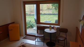 A compact room with a small table and two chairs, a radiator, and a sliding glass door leading to a garden.
