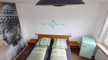 Une chambre avec un lit, une lampe fixée au mur, un radiateur et un petit réfrigérateur.