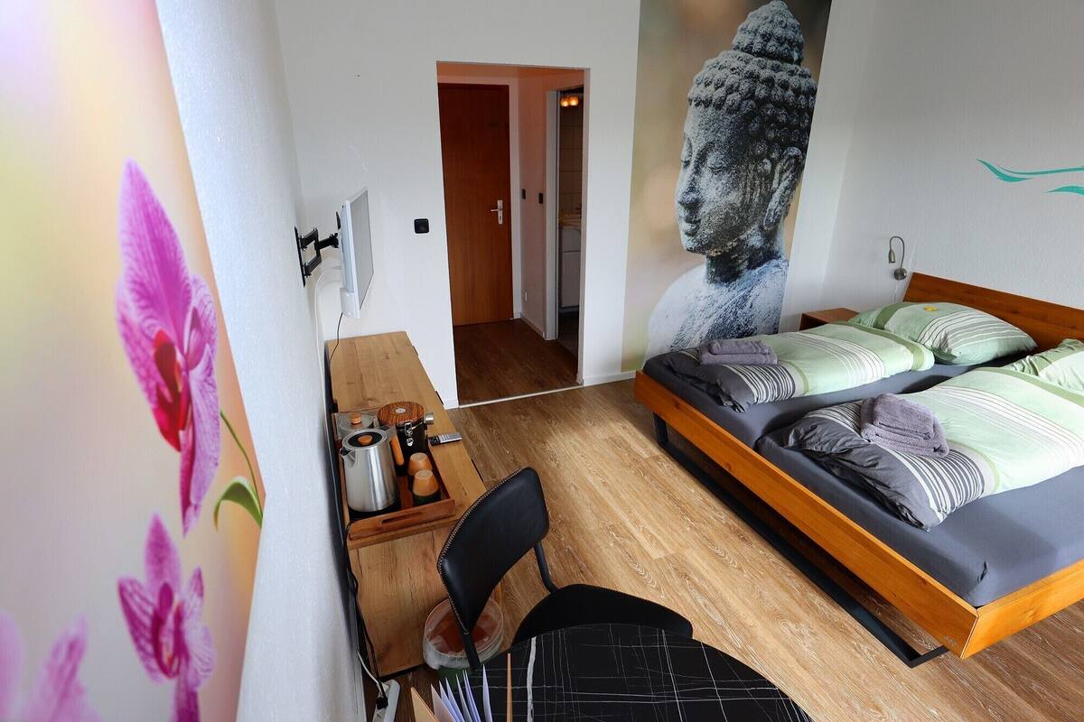 A bedroom with a bed, a desk with a chair, a wooden floor, and a wall with a painting.