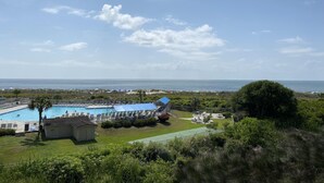A pool area with a view of the ocean, surrounded by greenery and a clear sky. - Ocean Front - Ocean Villas B329-Professionally Managed by HHIB&T Vacation Rentals (Hilton Head Island)
