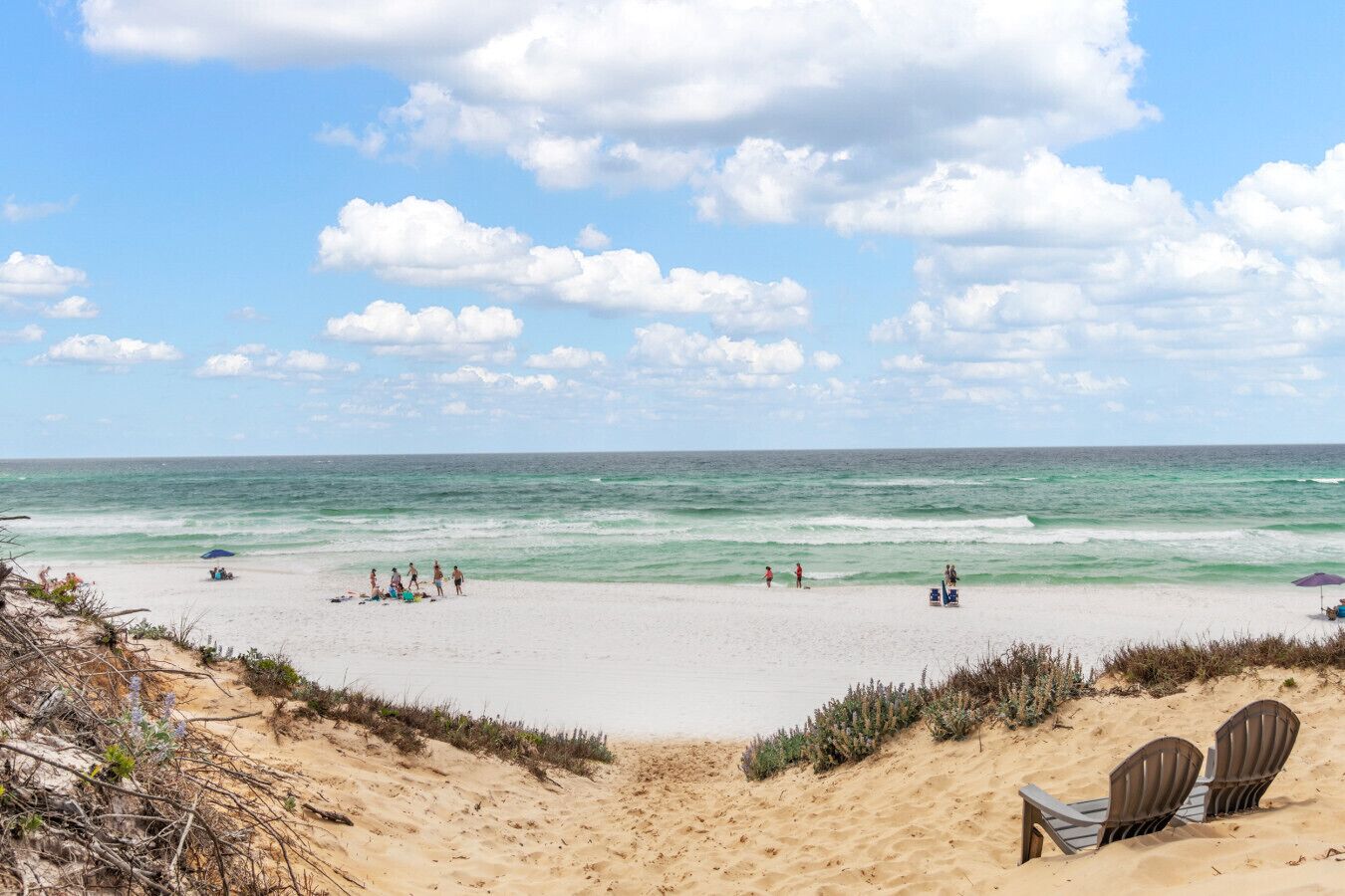 A beach with a sandy foreground, a few beach chairs, and people in the water.