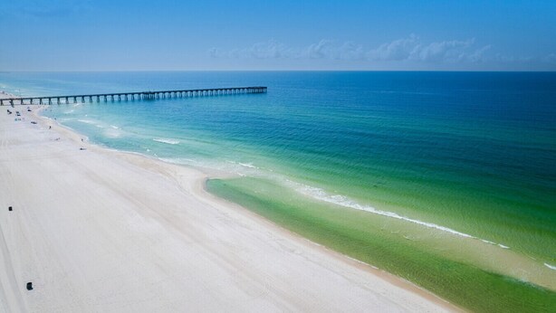Ein Strand mit einem Steg, der ins Meer führt, bewölkter Himmel und ruhiges Wasser.